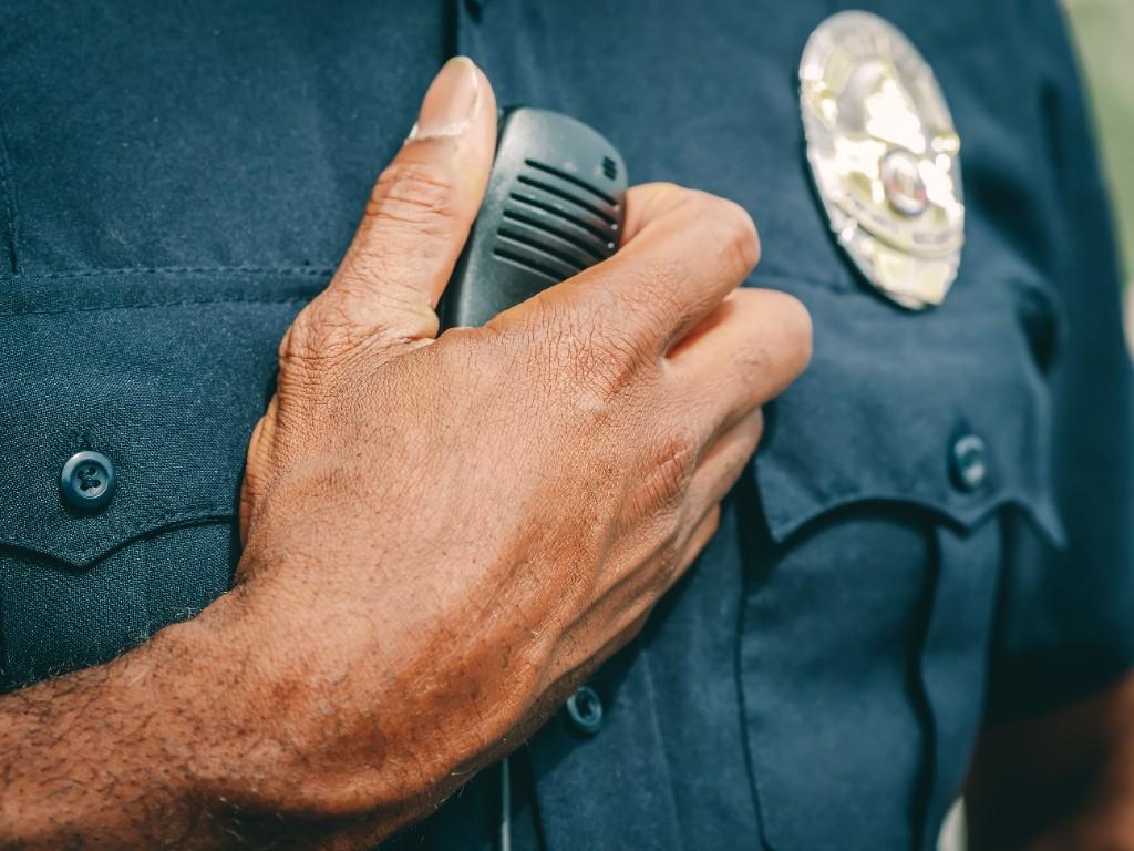 A police officer holding a radio microphone against a uniform with a badge