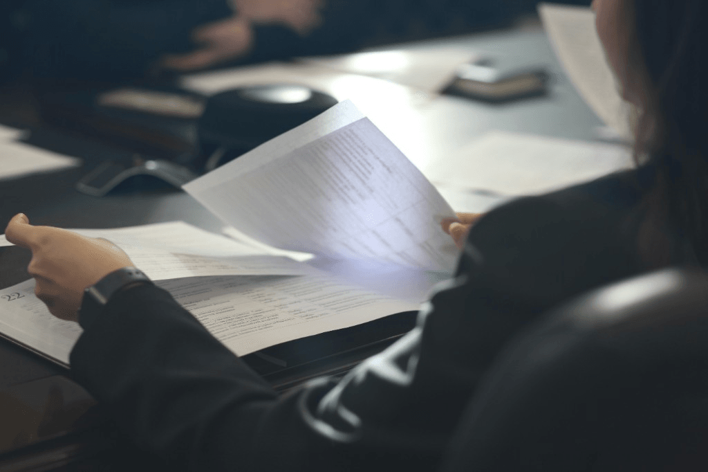 Professional reviewing a binder of formal documents at a dark conference table